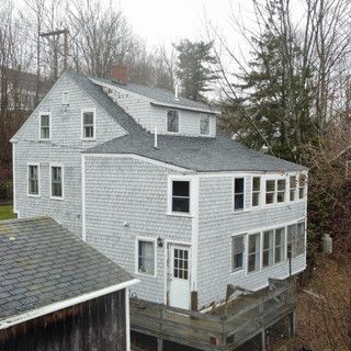 A large white house with a black roof is surrounded by trees.