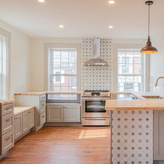 A kitchen with stainless steel appliances , wooden floors , white cabinets and a large island.