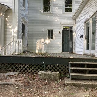 A white house with a wooden deck and stairs in front of it.