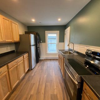 A kitchen with wooden cabinets , stainless steel appliances , a refrigerator , sink , and stove.