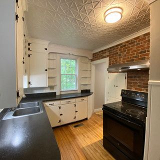 A kitchen with white cabinets , a black stove , a sink and a window.