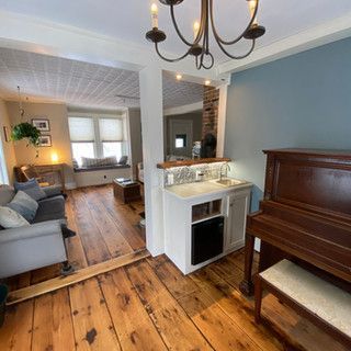 A living room with hardwood floors , a piano , a sink and a chandelier.