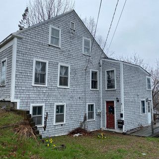 A large white house with a red door is sitting on top of a grassy hill.
