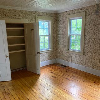 An empty room with hardwood floors , two windows , and a closet.