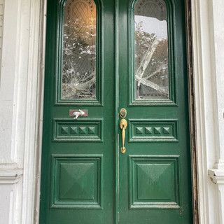 A pair of green doors with stained glass windows on a white building.