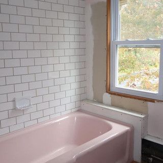 There is a pink bathtub in the bathroom next to a window.