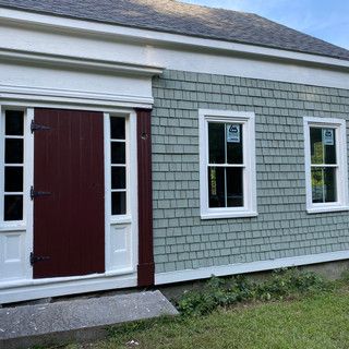 The front of a house with a red door and white windows.