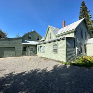 A large green house with a garage and a blue sky in the background.