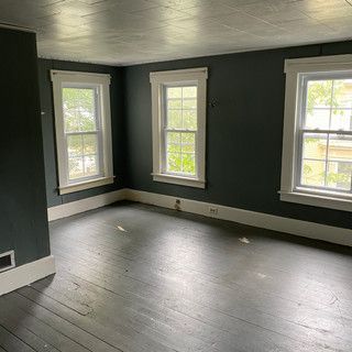 An empty room with a wooden floor and three windows.