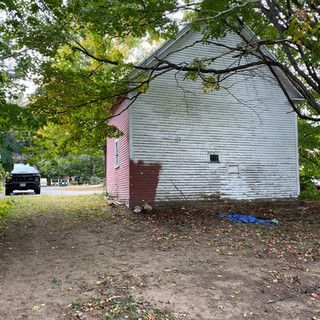 A white house with a red trim is sitting in the middle of a dirt field.