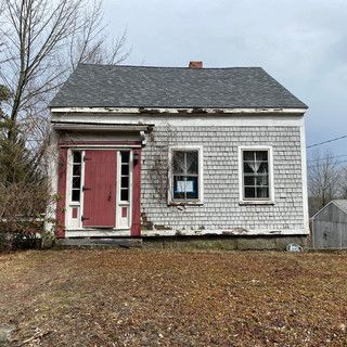 A small white house with a red door and windows is for sale.