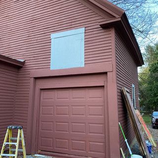 A red garage door is being painted on the side of a house.