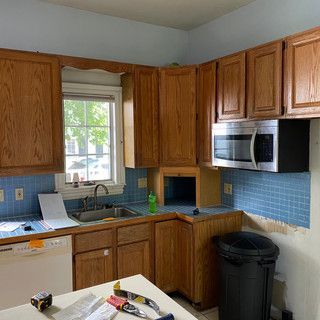 A kitchen with wooden cabinets , a microwave , a sink , and a window.
