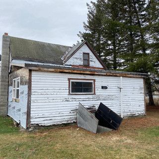 A small white house is sitting in the middle of a grassy field.