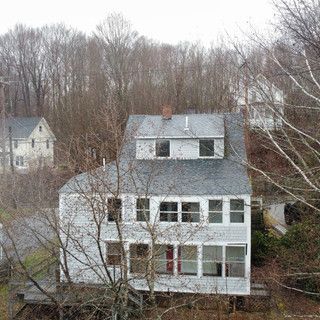 A white house with a black roof is surrounded by trees