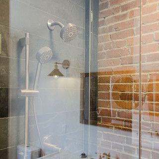 A bathroom with a glass shower door and a brick wall.