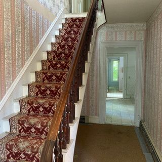 A staircase with a red carpet on the steps in a hallway.