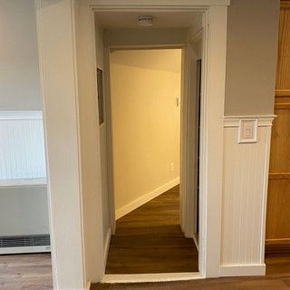 A hallway with a wooden floor and a white door leading to a room.