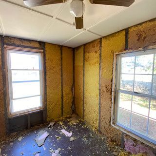 A room with a ceiling fan and two windows.
