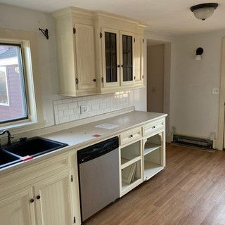 A kitchen with white cabinets , a sink , a dishwasher and a window.