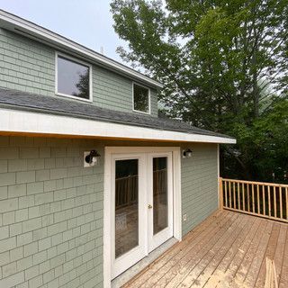 A green house with a wooden deck and sliding glass doors.