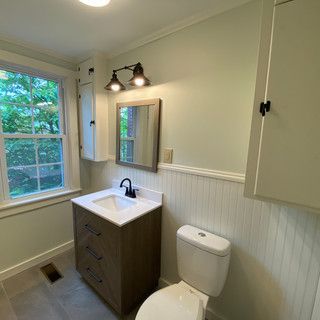 A bathroom with a sink , toilet , mirror and window.