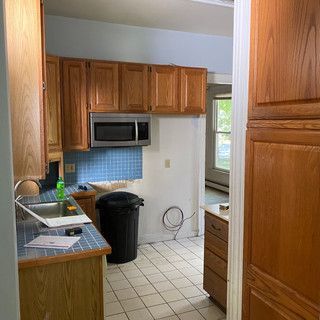 A kitchen with wooden cabinets , a sink , a microwave and a trash can.