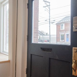 A black door with a window and a brick building in the background.