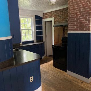 A kitchen with blue cabinets , a black stove and a brick wall.