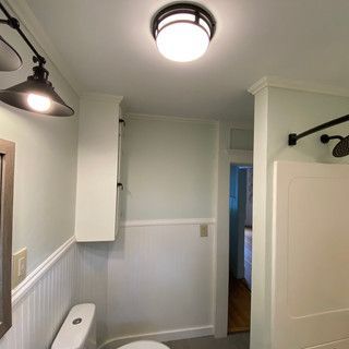 A bathroom with a toilet , mirror and ceiling light.