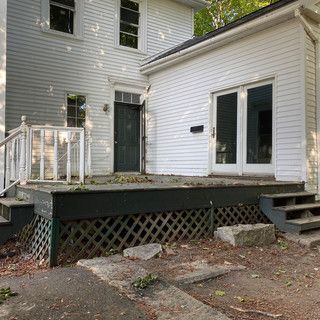 A white house with a deck and stairs in front of it.