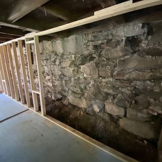 A stone wall is being framed in a basement.