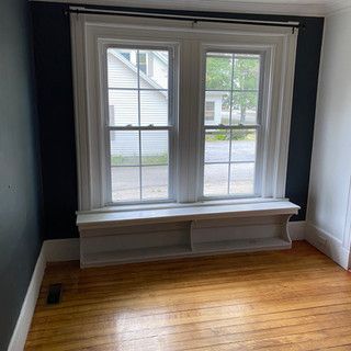 There is a window in the corner of the room with a bench underneath it.