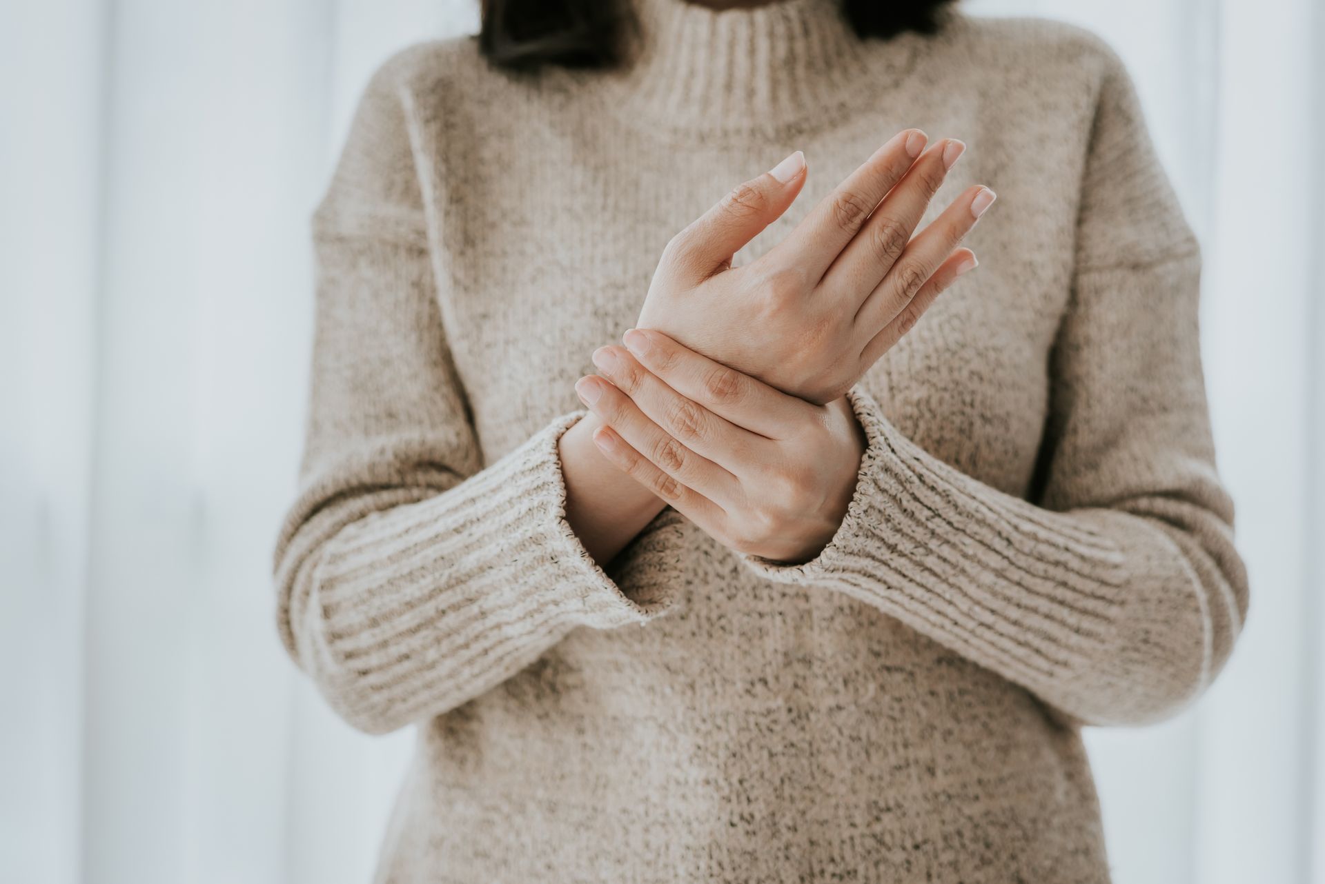 Person holding a wrist, wearing a beige sweater, suggesting wrist pain or discomfort