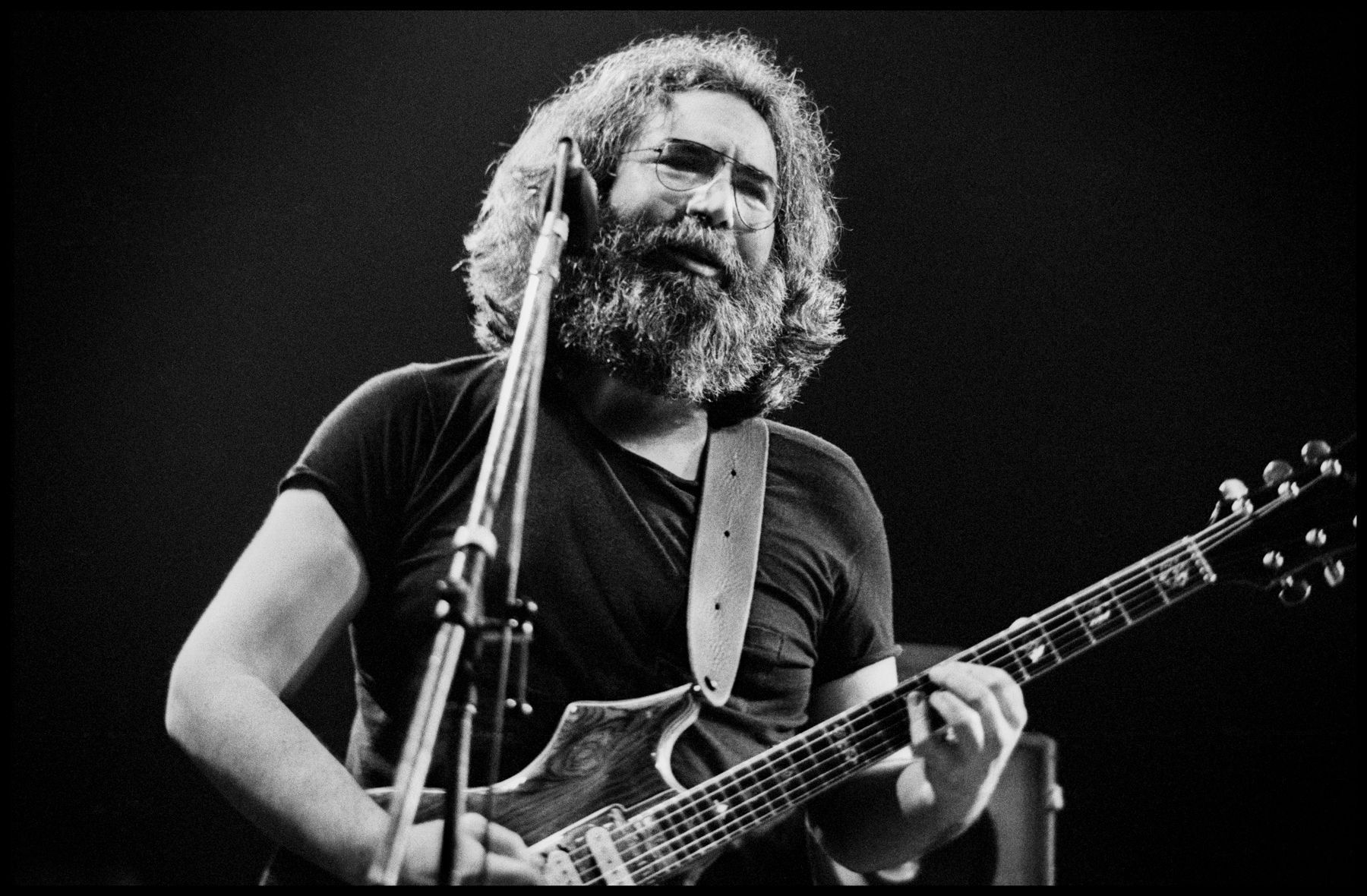 Black-and-white photo of a guitarist singing into a microphone on stage