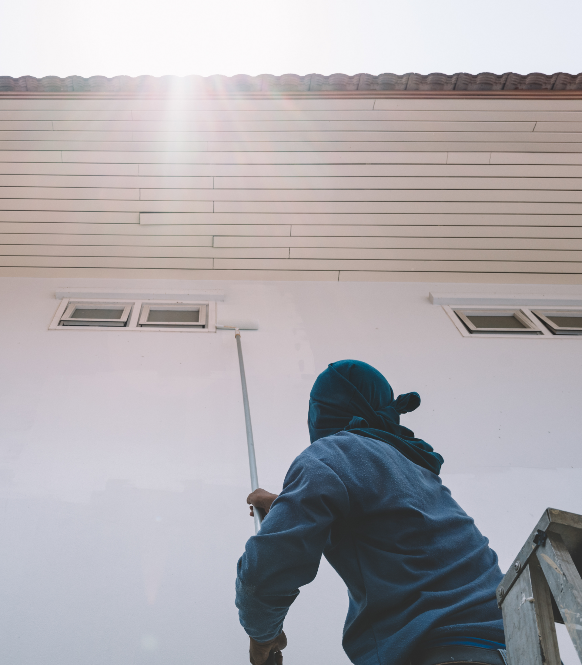 A man is painting the side of a building with a paint roller.