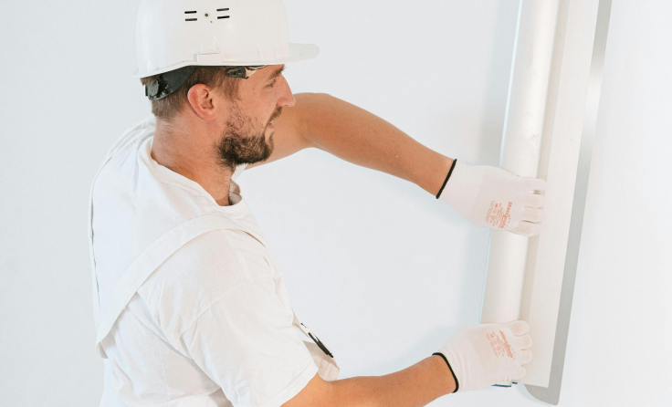 A man wearing a hard hat and gloves is plastering a wall.