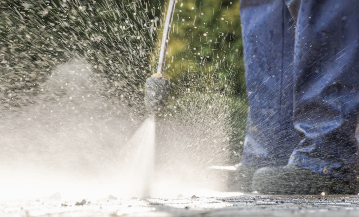 A person is using a high pressure washer to clean a sidewalk.