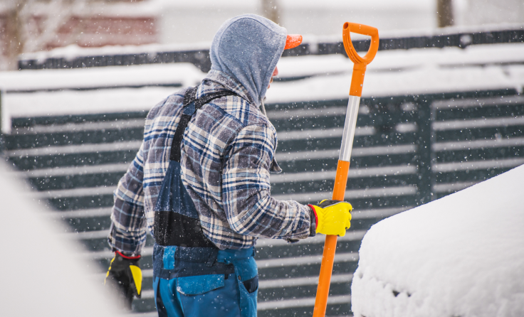 A man holding a shovel in snowy weather.