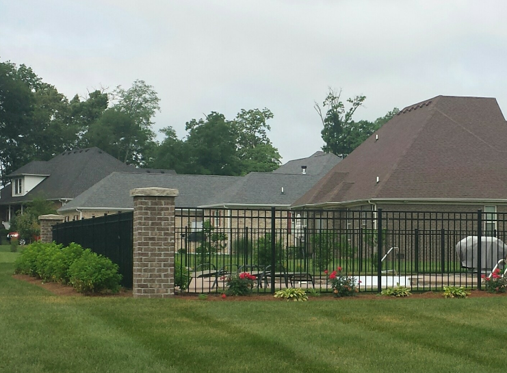 Black metal fence around a pool, with houses and green lawn in the background.