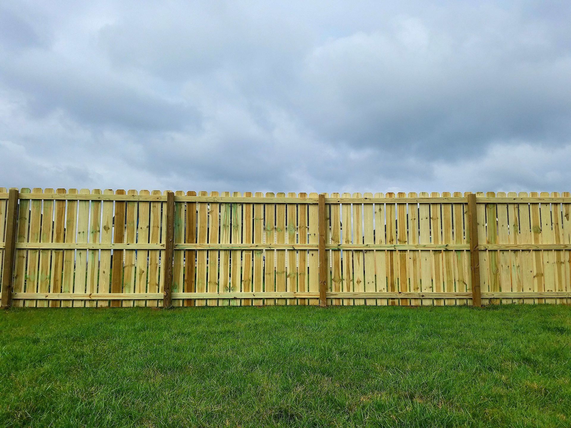 Wooden fence in green grass under a cloudy sky.