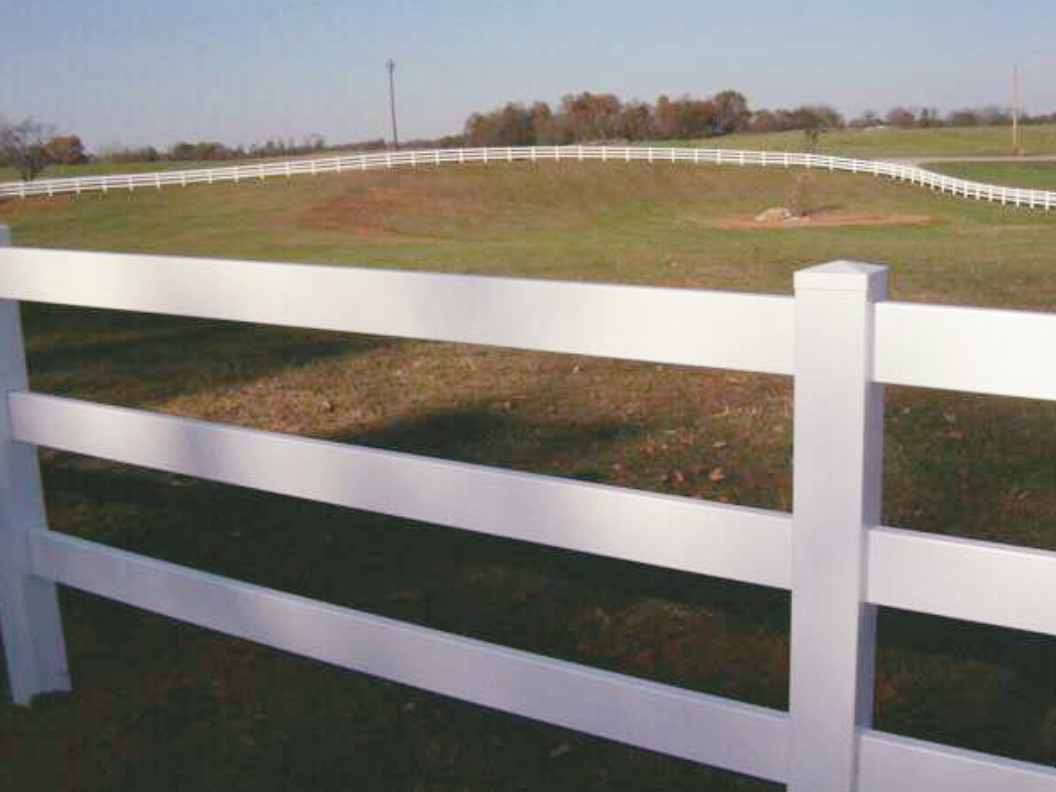 White fence in a grassy field with rolling hills under a blue sky.