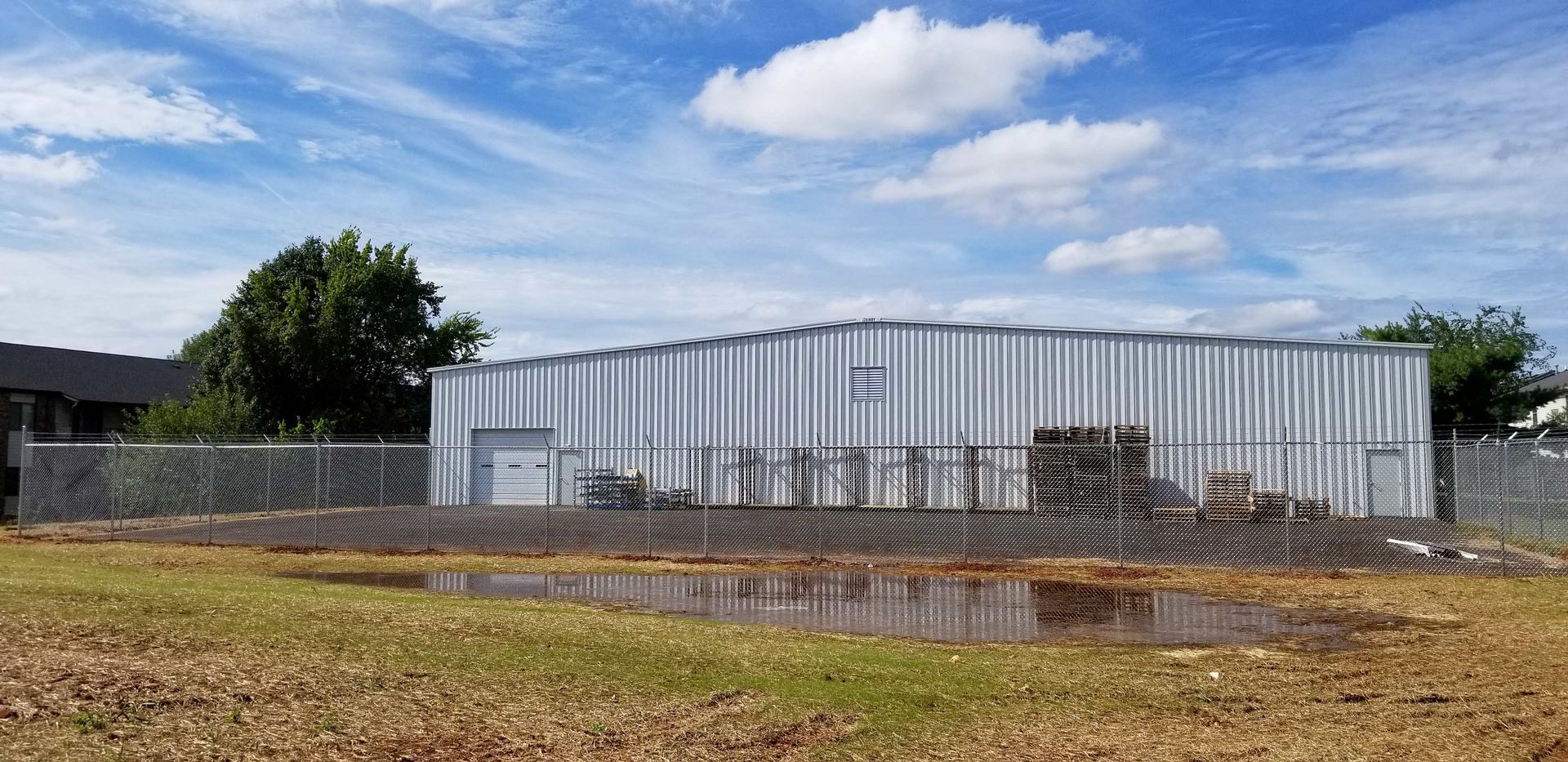 A metal building behind a chain link fence, under a blue sky with some clouds.