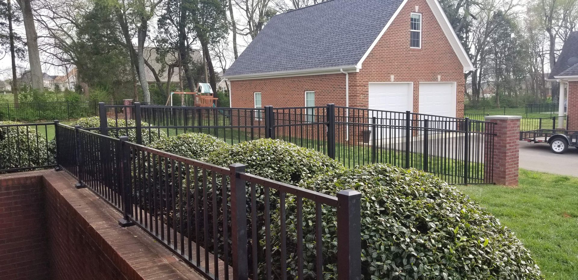 Black metal fence surrounds a garden with brick buildings and lush greenery in the background.