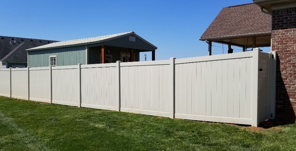 Beige vinyl fence in a green yard, separating houses. Bright blue sky.