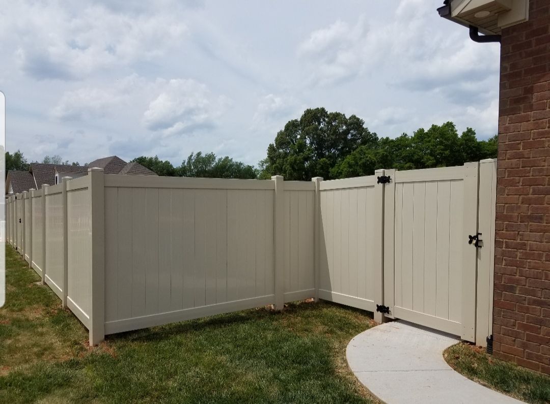 Tan vinyl fence with gate in a yard with grass and cloudy sky.