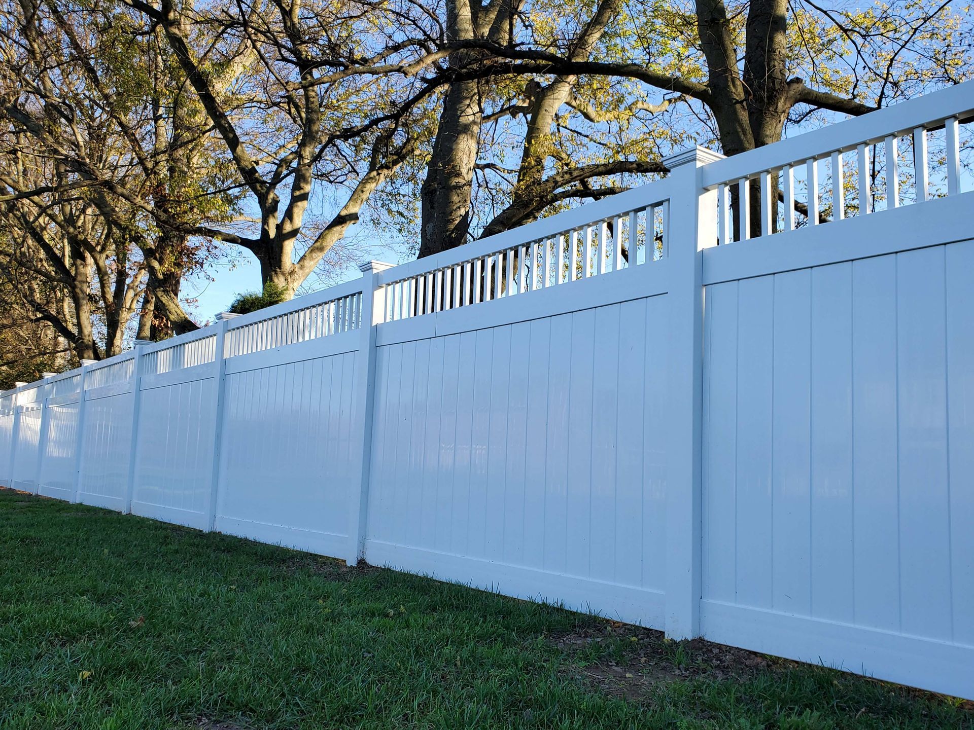 White vinyl fence in a grassy yard, with trees in the background.