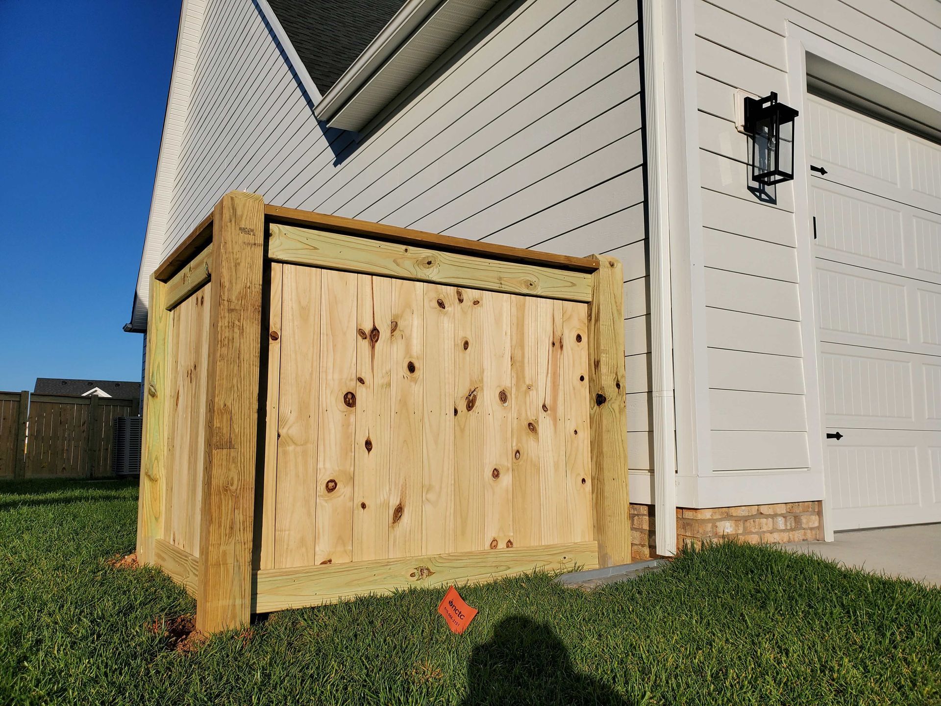 Wooden enclosure next to a house, concealing an object, with green grass and a blue sky.