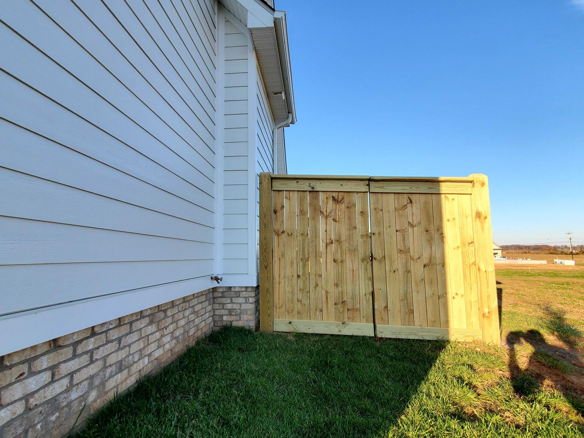 Wooden enclosure attached to a white house with green grass and a clear blue sky.