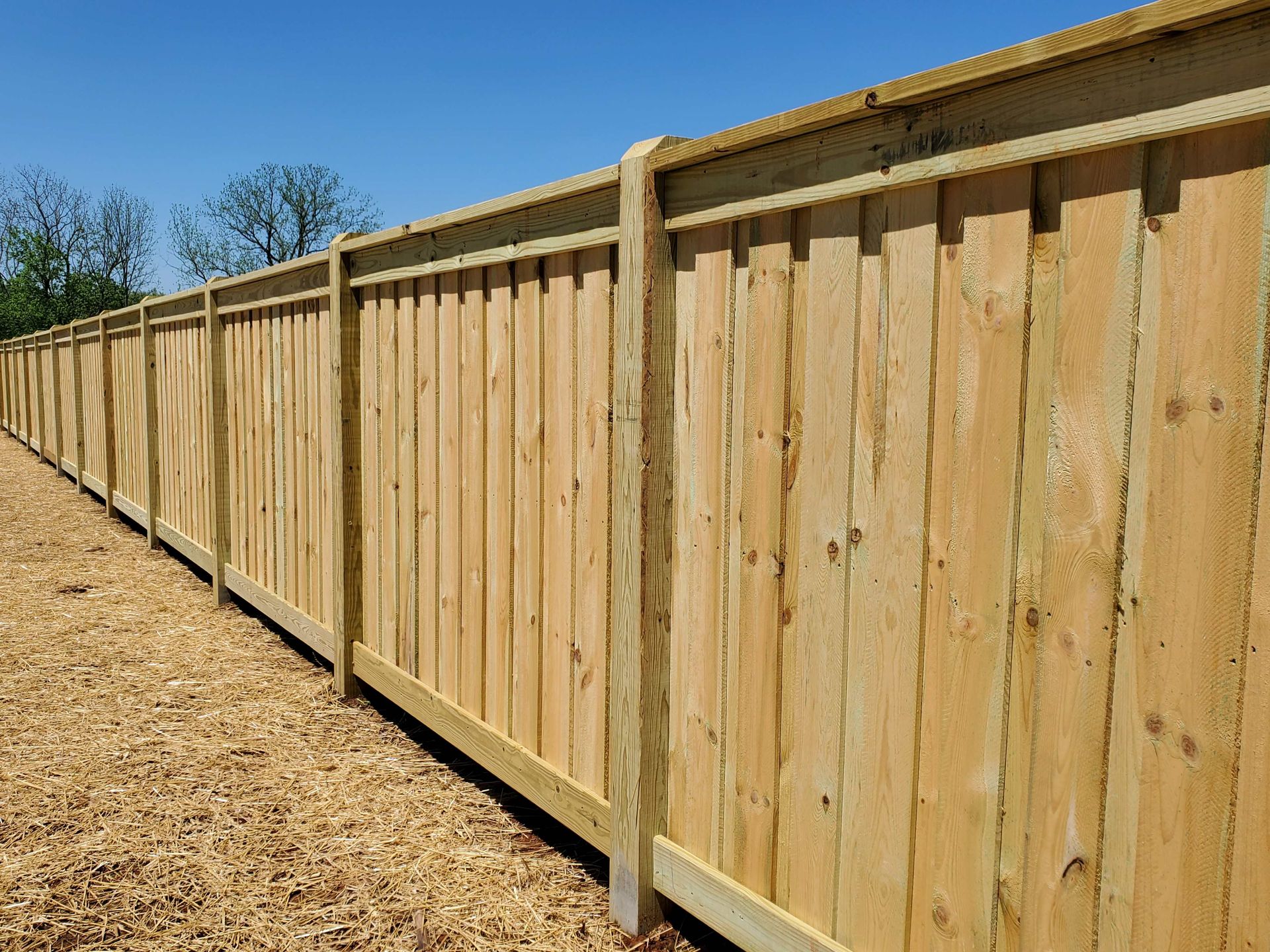 Wooden privacy fence extending into the distance on a gravelly ground under a blue sky.